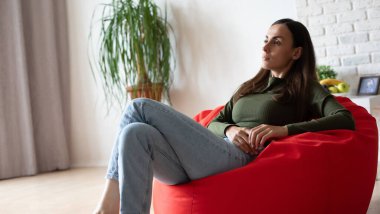 Güzel, genç, esmer bir kadın, günlük kıyafetleriyle evdeki fasulye çuvalında oturuyor ve rahatlıyor, dinleniyor, düşünüyor ve meditasyon yapıyor.