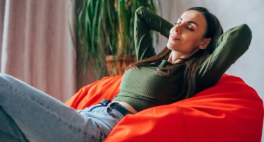 Güzel, genç, esmer bir kadın, günlük kıyafetleriyle evdeki fasulye çuvalında oturuyor ve rahatlıyor, dinleniyor, düşünüyor ve meditasyon yapıyor.
