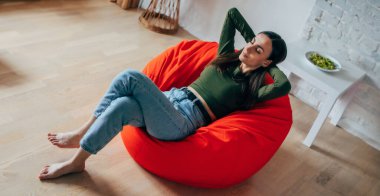 Güzel, genç, esmer bir kadın, günlük kıyafetleriyle evdeki fasulye çuvalında oturuyor ve rahatlıyor, dinleniyor, düşünüyor ve meditasyon yapıyor.