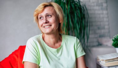 Orta yaşlı, mutlu, mutlu, rahat elbiseli bir kadının fotoğrafını çek. Evdeki kanepede dinleniyor ve gülüyor.