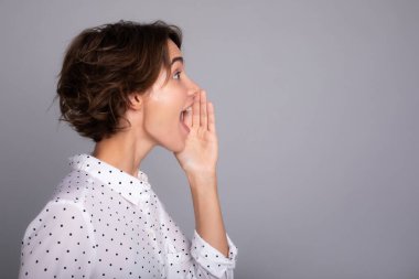 Gri arka plan stüdyosunda, şık giyinmiş güzel bir genç kadının portresi bağırıyor ya da dedikodu yapıyor..