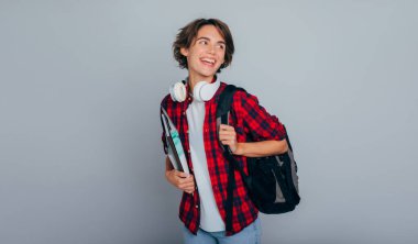 Neşeli, sevimli, akıllı ve modern bayan öğrenci kulaklıkları, sırt çantaları ve defterleri elinde, yan tarafa bakıyor ve gülüyor. Üniversite, öğrenim, okul, eğitim, üniversite, sınıflar, bilgi.
