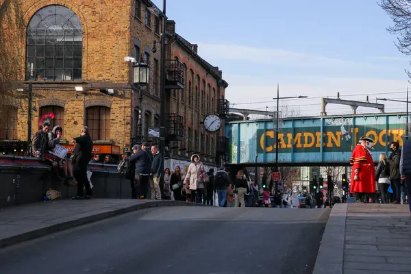 Londra, Birleşik Krallık, Ocak 12022: Camden Lock Köprüsü 'nde kırmızı ceket giymiş bir adam ve köprüde oturan serseriler