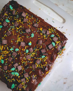 Lezzetli ev yapımı, kremalı, çikolata parçalı, yeşil ve sarı parçalı, beyaz tahtada servis edilen, ev yapımı, sade çikolatalı pasta.