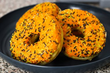 Halloween themed donuts with orange icing, black green and white sprinkles clipart