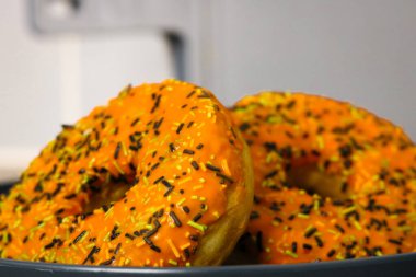 İki Cadılar Bayramı temalı donut, turuncu kremalı, siyah yeşil ve beyaz serpiştirilmiş.