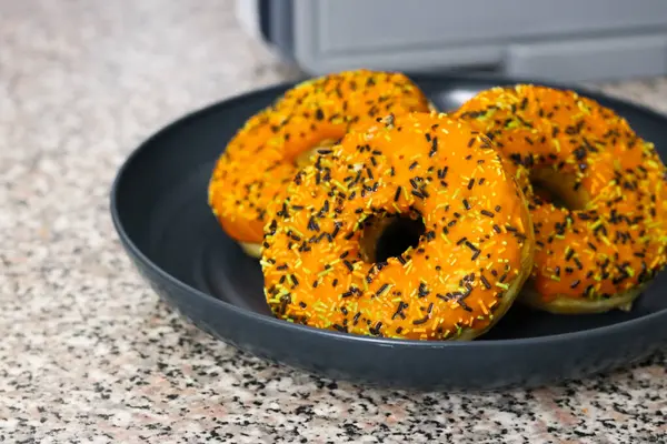Üç Cadılar Bayramı temalı donut, turuncu kremalı, siyah yeşil ve beyaz serpiştirilmiş.