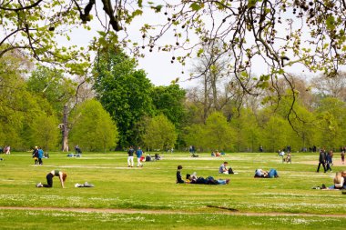 Londra, İngiltere, 30 Nisan 2023: Kensington Bahçeleri çimenlerin üzerindeki insanların manzarası, bazıları güneşli güzel bir günde egzersiz yaparken dinleniyor