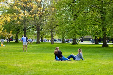 Londra, İngiltere, 30 Nisan 2023: Kensington Bahçeleri çimenlerde oturan iki arkadaşla güneşli güzel bir günün tadını çıkarıyorlar.