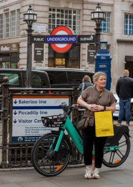 Piccadilly Sirki 'nde elinde çantasıyla, metro girişinde bisikletin yanında duran bir kadın..