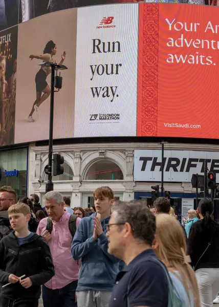 Piccadilly Sirki 'nde insanlar yoğun bir öğleden sonra büyük ekranlarla karşıdan karşıya geçmek için bekliyor..