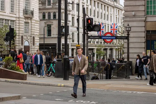 Piccadilly Sirki 'ni geçerken şık giyinmiş bir adam. Arka planda yer altı tabelası ve insanlar var.
