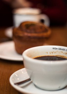Ön planda koyu kahve, bulanık tarçınlı çörek ve arka planda başka bir kupa.