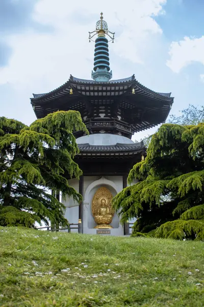 Londra, İngiltere, 24 Mayıs 2023: Battersea Park 'taki Londra Barış Pagoda bazı ağaçlar ve arkadaki mavi gökyüzü tarafından çerçevelenmiş