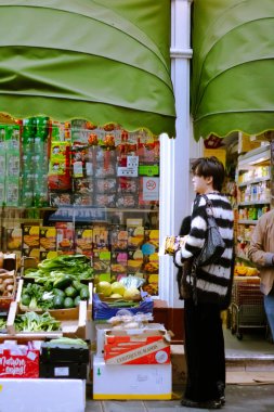 Çin Mahallesi 'ndeki bir mini marketin önünde bir sürü taze ürünle bekleyen kişi.