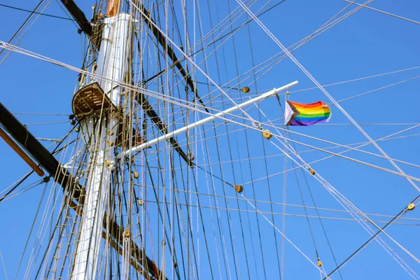 Arka planda mavi gökyüzü olan yelken direğinde LGBT Gurur bayrağı