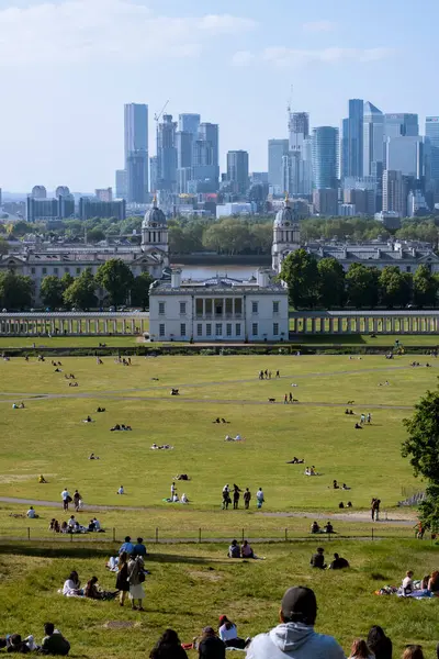 Greenwich Park 'ın tepesinden, çimlerin üzerinde insanlar, ve arka planda Canary Wharf