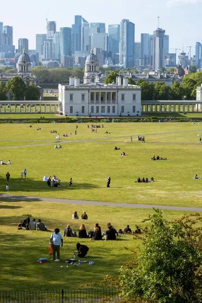 Greenwich Park 'ın tepesinden, çimlerin üzerinde insanlar, ve arka planda Canary Wharf
