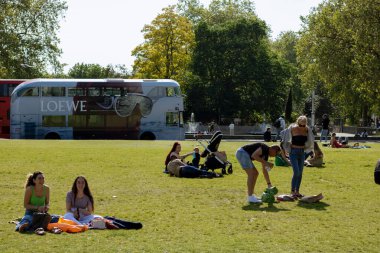 People sitting on the grass by the Marble Arch with a branded Loewe double decker in the background clipart