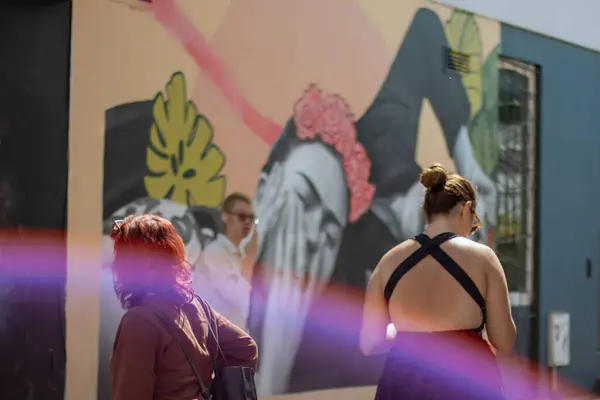 Portobello Market 'te arka planda Frida Khalo Sokak Sanatı, bir ışık huzmesi ve yanından geçen insanlar.