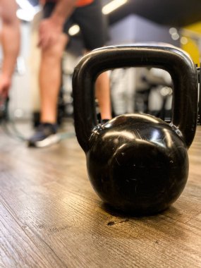 Ön planda spor ağırlığı ve arka planda egzersiz yapan birinin bacakları.