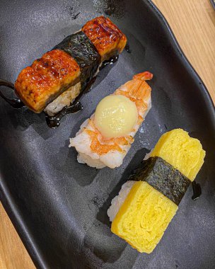 Çeşitli suşi somonlarıyla siyah seramik tepsi, deniz ürünleri rulosu ve Japon restoranında ızgara biftek iştah açıcı yemek.