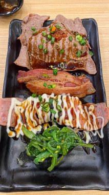 Çeşitli suşi somonlarıyla siyah seramik tepsi, deniz ürünleri rulosu ve Japon restoranında ızgara biftek iştah açıcı yemek.