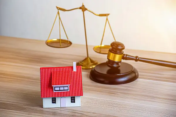 Ev modeli, çekiç yargıç tokmağı beyaz duvar arka planlı ahşap masada. İpotek, iflas konsepti. Ödenmemiş borçları veya yükümlülükleri ödeyemeyen kişi, ipotek ödemesini durdurur.