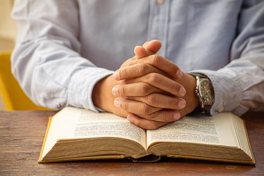 Hristiyan adam İncil 'le Tanrı' ya dua ediyor. İyiliğe inan. Tanrı 'nın daha iyi bir hayat dilemesi için tahta bir masada el ele tutuşmak. Dua ve ibadet kavramı.