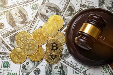 Üzerinde Bitcoin kripto para sembolü olan altın bir sikke ve arka planda 100 dolarlık banknotlar bulunan bir yargıç tokmağı.