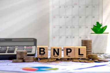 Şimdi satın almak için daha sonra ödeme, online alışveriş konsepti, BNPL metin ve para yığını ile ahşap küp blok, alışveriş arabası ve saat bulanık beyaz hesap makinesi