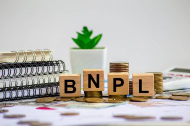 Şimdi satın almak için daha sonra ödeme, online alışveriş konsepti, BNPL metin ve para yığını ile ahşap küp blok, alışveriş arabası ve saat bulanık beyaz hesap makinesi