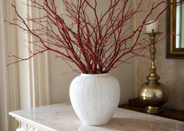 A photo of a still life scene featuring a white vase with a unique, textured finish, a table, and another smaller decorative object with a similar textured finish. The vase is white and contains thin, red-stemmed plants. The table has a marble-like f clipart