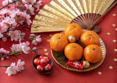 A still life photo featuring a traditional Asian-inspired arrangement with a focus on oranges, a fan, and a branch of pink cherry blossom flowers. The oranges are arranged on a plate, with the fan nearby and cherry blossoms scattered around the table clipart