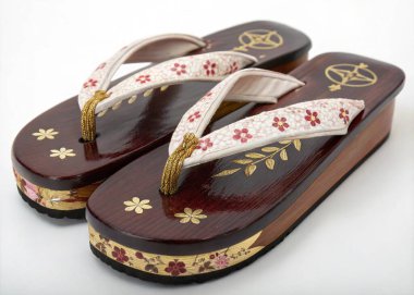 A photo of a pair of traditional Japanese wooden sandals with a rich, dark brown base, featuring intricate floral and leaf patterns in gold accents. The sandals are crafted from wood, showcasing a smooth finish, and the straps are also made of a simi clipart