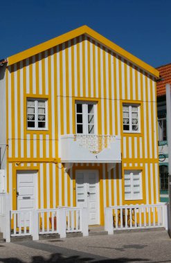 Portekiz 'de bir köyde sarılı, beyaz çizgili güzel bir ev. Bu köy evi sahile yakın ve yoldaki birkaç renkli evin arasında duruyor.