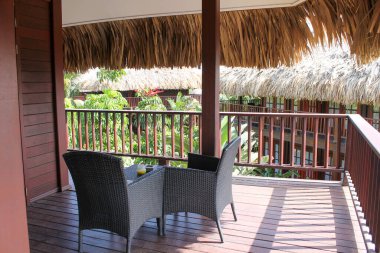 Tropik bir adada, bir sürü ahşap, bahçe mobilyası ve palmiye yapraklı çatısı olan güzel bir balkon.