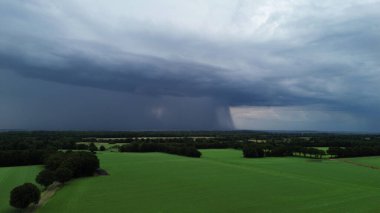 Çayırların üstündeki kara bulutlardan yağmur yağıyor.