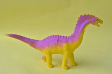 Çocuk oyuncağı dinozor sarı arka planda izole edilmiş.