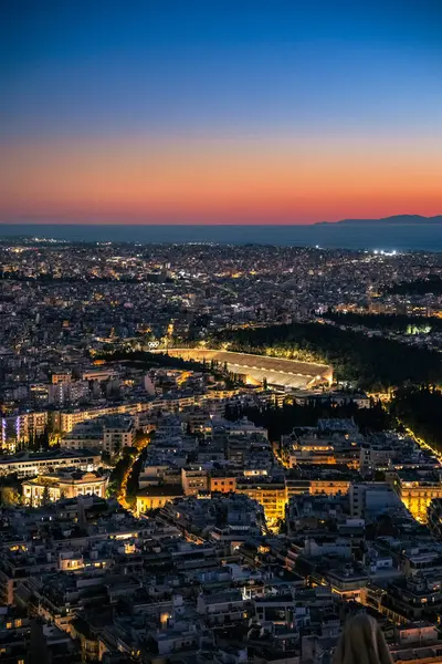 Günbatımında Yunanistan 'ın Atina kentindeki Panathenaic stadyumuyla birlikte Atina' nın aydınlık ufuk çizgisi üzerinde dikey görüş. Antik Olimpiyat Stadyumu