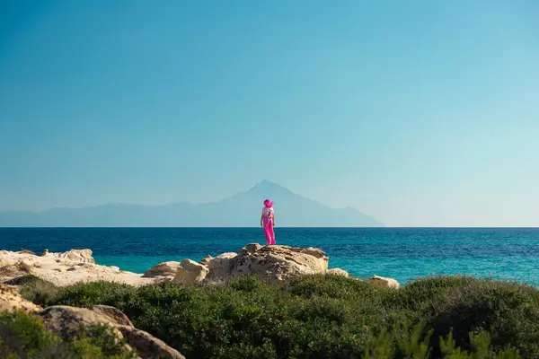 Karydi sahilinden Athos Dağı 'na doğru manzaranın tadını çıkaran kız, Sithonia Yarımadası, Chalkidiki, Yunanistan Ege Denizi' nde Yaz