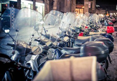 Lucca, Italy - December 2022: Scooter motorcycles parked next to each other at night on a street can be a common sight in urban areas where scooter-sharing services are popular.