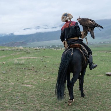 Issyk Kul, Kyrgyzstan - May 2022: Eagle trainer on a horse and his golden eagle, skilled in training eagles for hunting, using traditional techniques passed down through generations