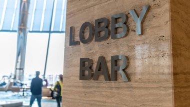 Mermer duvardaki otel tabelasında lobi ve bar yazıyor. Arka planda tanımlanamayan kişilerle seçmeli odak