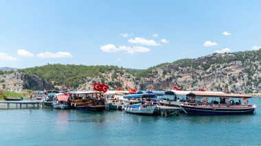 Dalyan, Ortaca, Mugla, Türkiye - Haziran 2022: Dalyan nehrinde turistleri taşıyan tekneler, antik Lycian kaya mezarları, çarpıcı Iztuzu plajı ve ünlü çamur banyosunun yanından geçiyor.