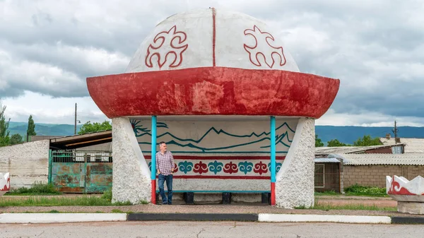 stock image Kyrgyzstan - May 2022: Man waiting at the Kyrgyz bus stop, which is in the shape of traditional central asian kalpak hat.