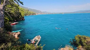 Akyaka, Mugla, Türkiye - 20 Ağustos 2023: Akyaka köyünün deniz kıyısında yüzen insanlar, manzaralı kıyı şeridi ve çarpıcı doğal çevresiyle popüler turistik beldeler