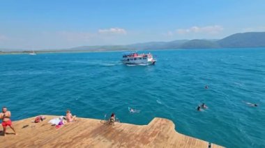 Akyaka, Mugla, Türkiye - 20 Ağustos 2023: Akyaka köyü kıyılarından geçen bir tur teknesi, manzaralı kıyı şeridi ve çarpıcı doğal çevresiyle popüler turistik durak