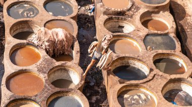 Fez, Fas - 10 Eylül 2022: Geleneksel bir tabakhanede deri ölüyor. Deri tabakhanelerdeki boya kaplarında tabakçı olarak çalışan adamlar. Bronzlaşma çukurları deri boyalarla doludur.