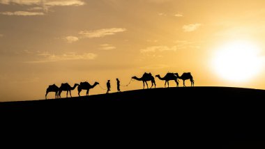 Berberi liderliğindeki iki Berberi 'nin silueti Sahra Çölü, Fas' ta gün batımında kum tepelerinde birbirleriyle karşılaştılar.
